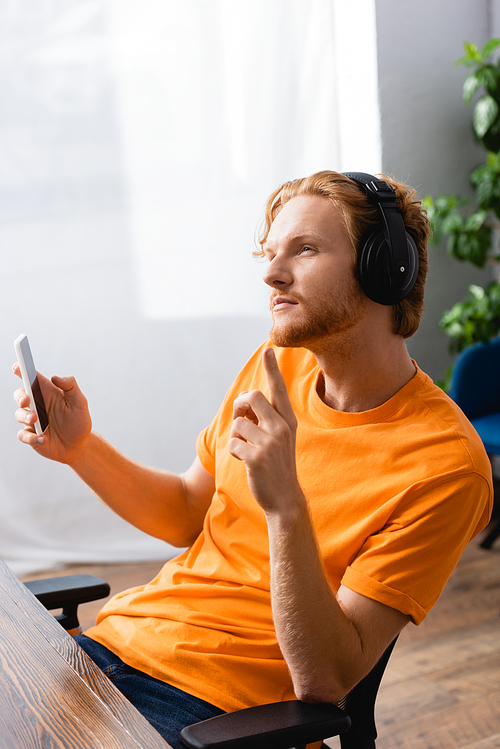 thoughtful man in wireless headphones showing idea gesture while holding smartphone
