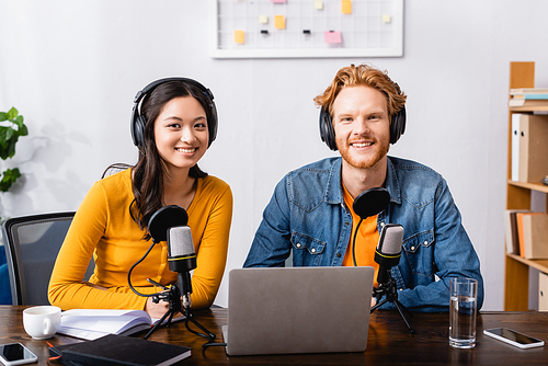 young radio hosts in wireless headphones  near microphones in studio