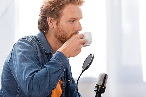 young redhead radio host in denim shirt drinking coffee near microphone