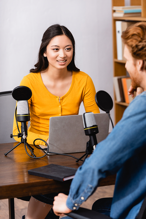 selective focus of young asian radio host using laptop while interviewing man in studio