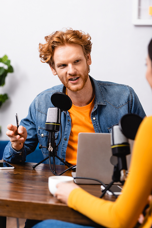 selective focus of woman and redhead interviewer holding pen and talking near microphone