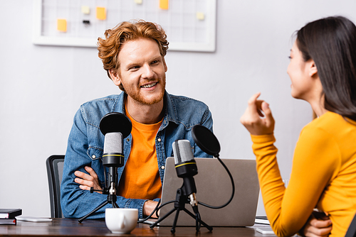 redhead broadcaster looking at brunette woman during interview in radio studio