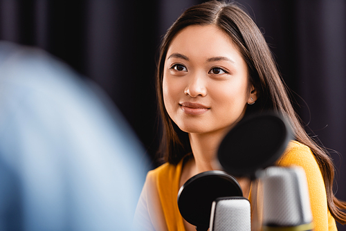 selective focus of young, brunette asian broadcaster near microphone in radio studio