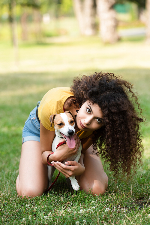 Selective focus of young woman sitting on grass and embracing dog