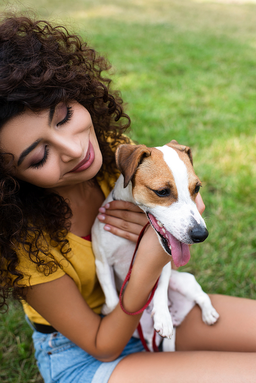 High angle view of young woman sitting on grass and looking at dog