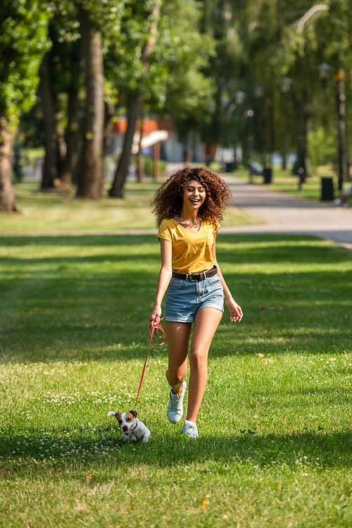 Selective focus of young woman walking and keeping dog on leash