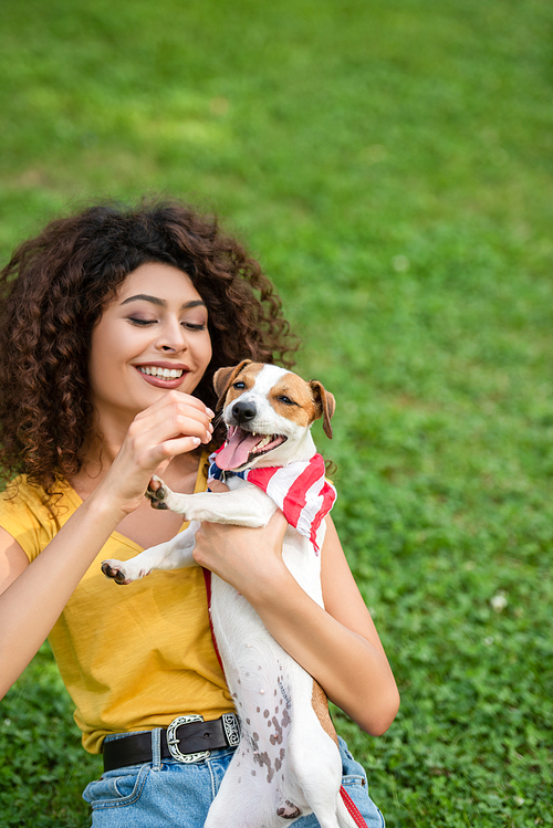 Selective focus of young woman sitting and holding dog with american flag bandana