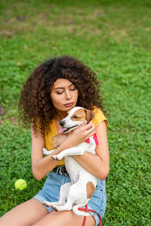 Selective focus of young woman sitting and holding dog on grass