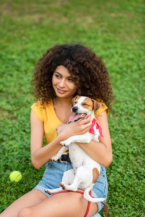 Selective focus of young woman sitting on grass with dog and looking away