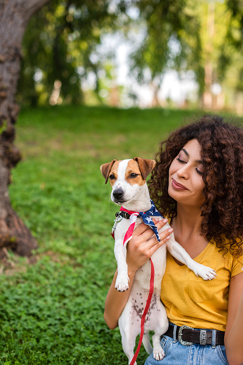 Selective focus of young woman holding dog wearing american flag bandana