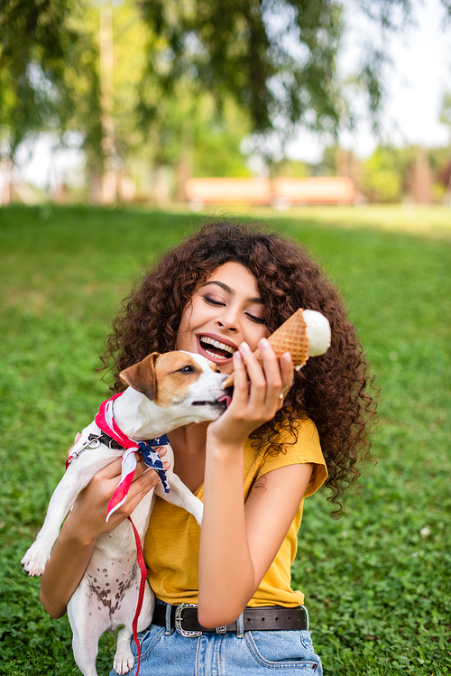 Selective focus of woman sitting on grass with ice cream and holding dog