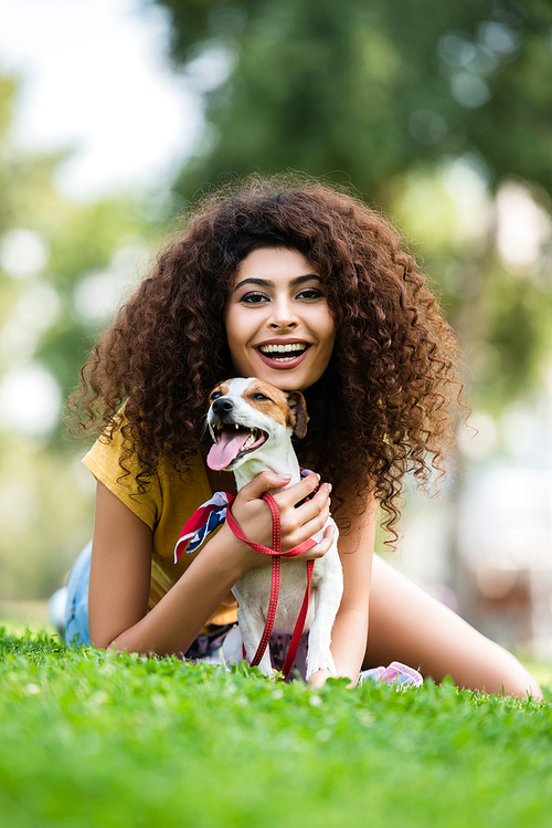 excited woman laughing and  while lying with jack russell terrier dog on green lawn