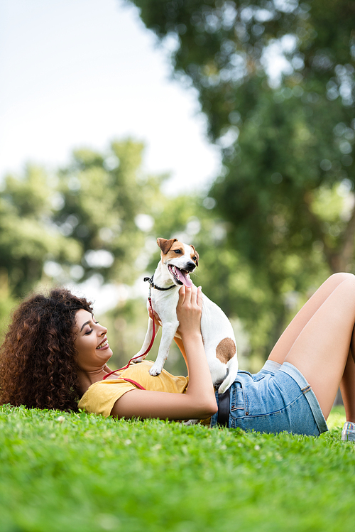 joyful woman in summer outfit lying on green lawn with jack russell terrier dog