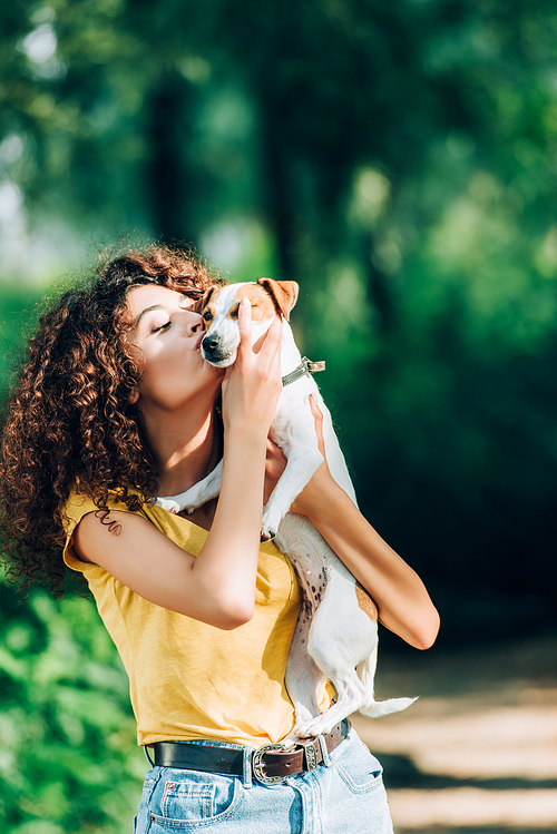 young woman in summer outfit kissing jack russell terrier dog in park