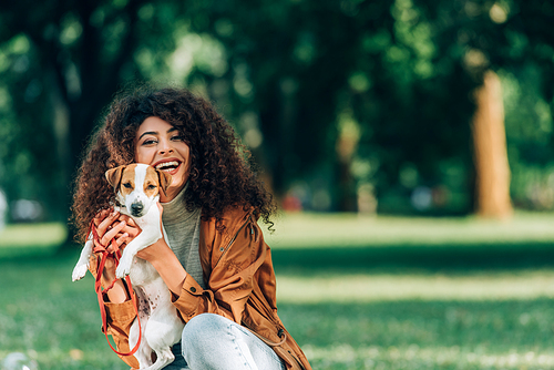 Young woman in raincoat holding jack russell terrier and  in park