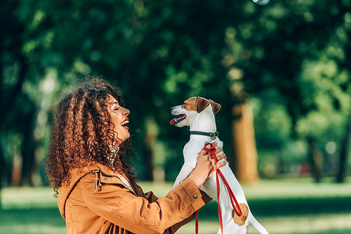 Side view of young curly woman holding jack russell terrier in park