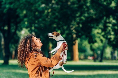 Side view of curly woman holding jack russell terrier in park