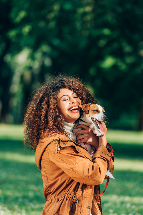 Young woman in raincoat hugging jack russell terrier in park