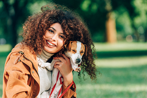 Young woman in raincoat  while hugging jack russell terrier in park