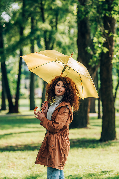 Curly woman in raincoat holding umbrella and  in park