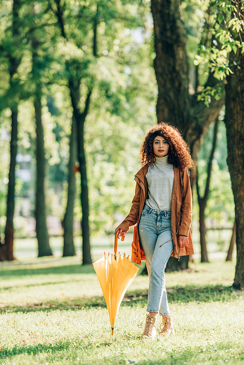 Selective focus of curly woman holding umbrella while strolling in park