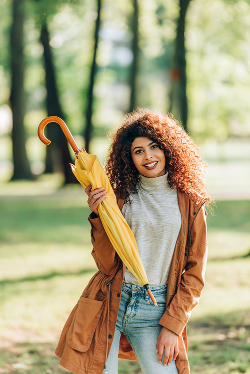 Young woman in raincoat holding umbrella and  in park