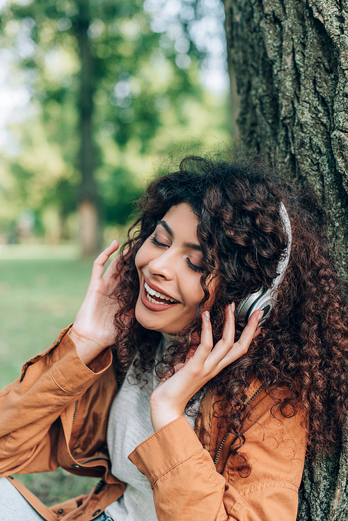 Young woman with closed eyes listening music in headphones near tree in park