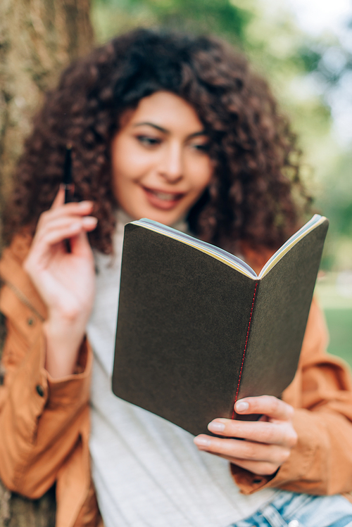 Selective focus of young woman looking at notebook in park