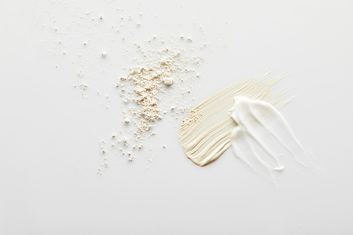 Top view of face powder, cosmetic and tone cream brushstrokes on grey background