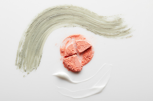Top view of cosmetic clay and cream brushstrokes with blusher on grey background