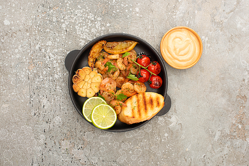 top view of fried shrimps with grilled toasts, vegetables and lime near sauce on grey concrete background
