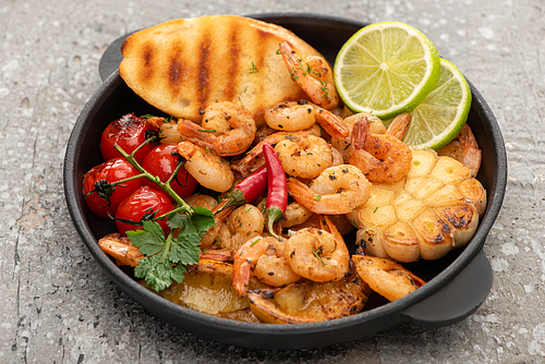 fried shrimps with grilled toasts, vegetables and lime on grey concrete background