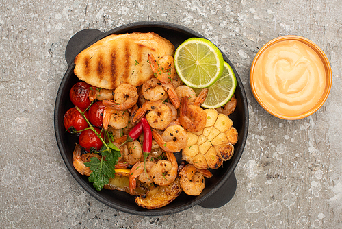 top view of fried shrimps with grilled toasts, vegetables and lime with sauce on grey concrete background