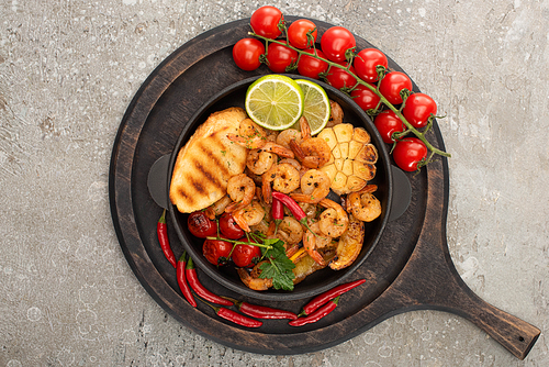 top view of fried shrimps with grilled toasts, vegetables, cherry tomatoes and lime on wooden board on grey concrete background