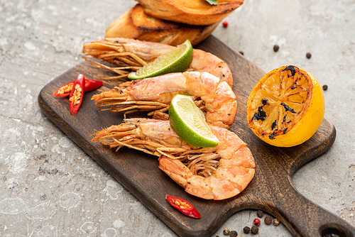 fried shrimps with grilled toasts, lemon and lime on wooden board on grey concrete background