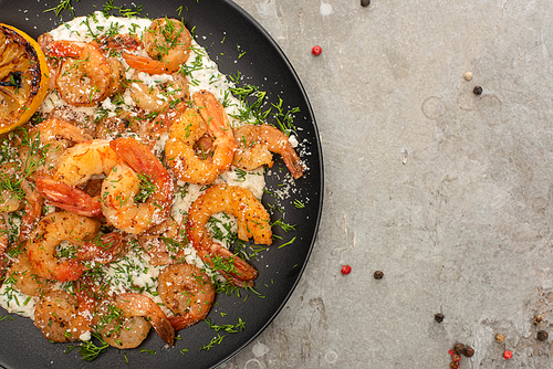 top view of fried shrimps in sauce with dill and lemon in frying pan on grey concrete background