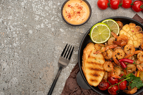 top view of fried shrimps with sauce, fork, grilled toasts, s and lime on grey concrete background