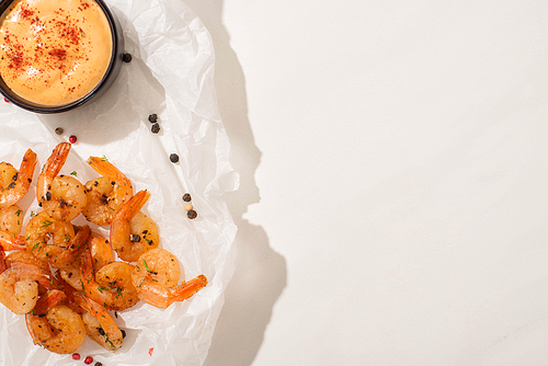 top view of fried shrimps on parchment paper with pepper, sauce on white background