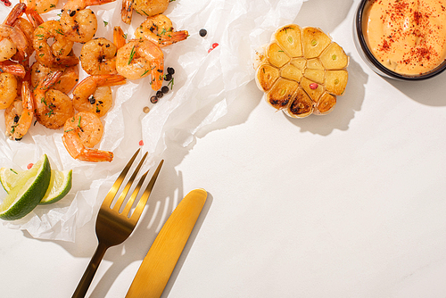 top view of fried shrimps on parchment paper with cutlery, grilled corn, pepper, sauce and lime on white background