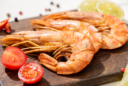 close up view of fried shrimps on wooden board with cherry tomatoes and lime