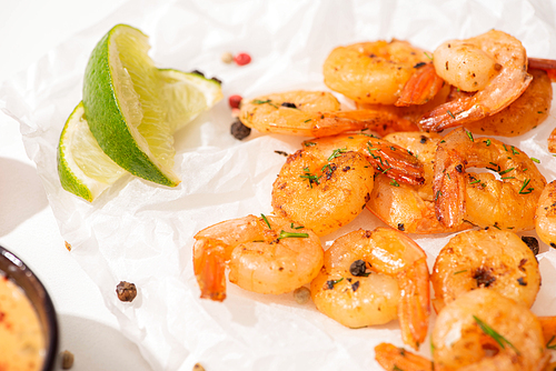 close up view of fried shrimps with lime and pepper on white parchment paper