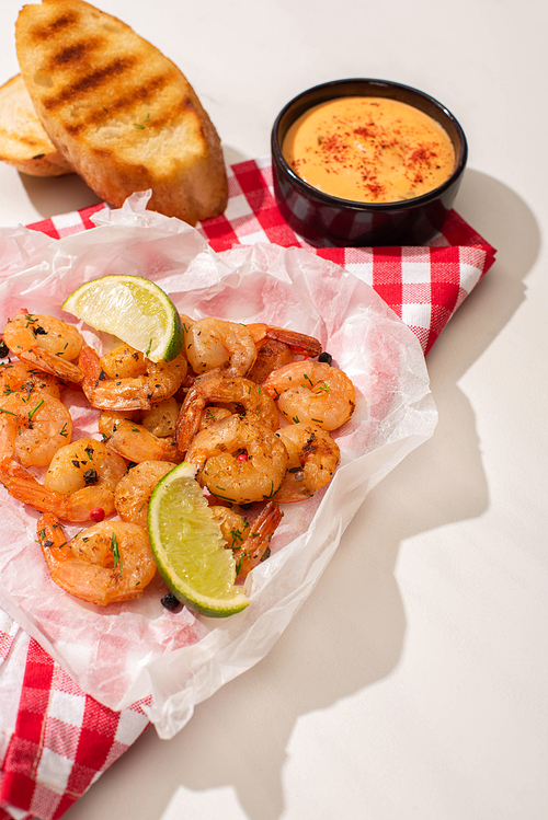 fried shrimps on parchment paper with sauce, bread toast and lime on white background with red plaid napkin