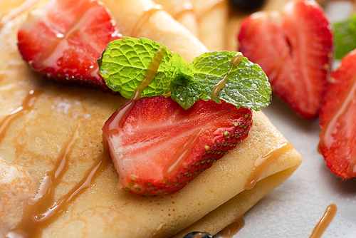 close up view of tasty crepes with strawberries and mint