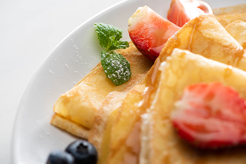 close up view of tasty crepes with blueberries, strawberries and mint on plate