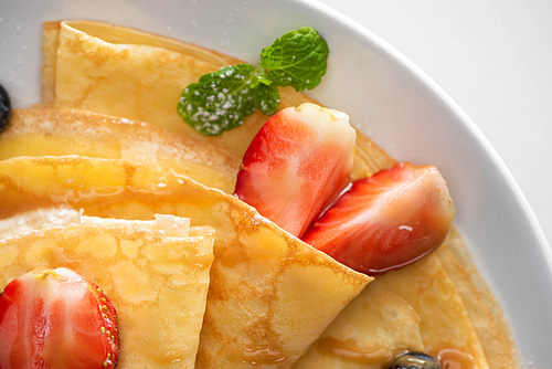 close up view of tasty crepes with strawberries and mint on plate