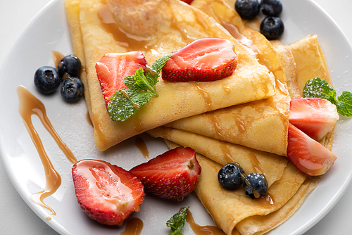close up view of tasty crepes with blueberries, strawberries and mint on plate