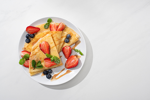 top view of tasty crepes with blueberries, strawberries and mint on plate