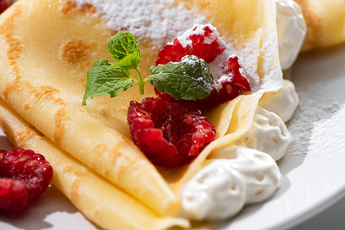 close up view of tasty crepes with raspberries and whipped cream on plate