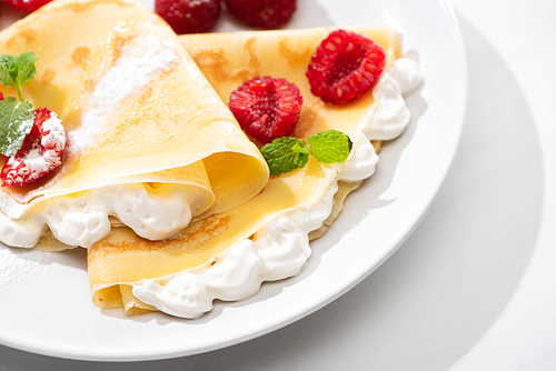 close up view of tasty crepes with raspberries and whipped cream on plate