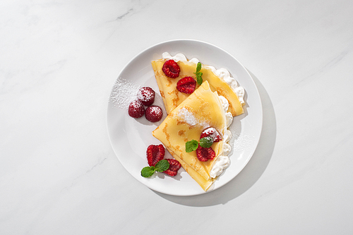 top view of tasty crepes with raspberries and whipped cream on plate on grey background